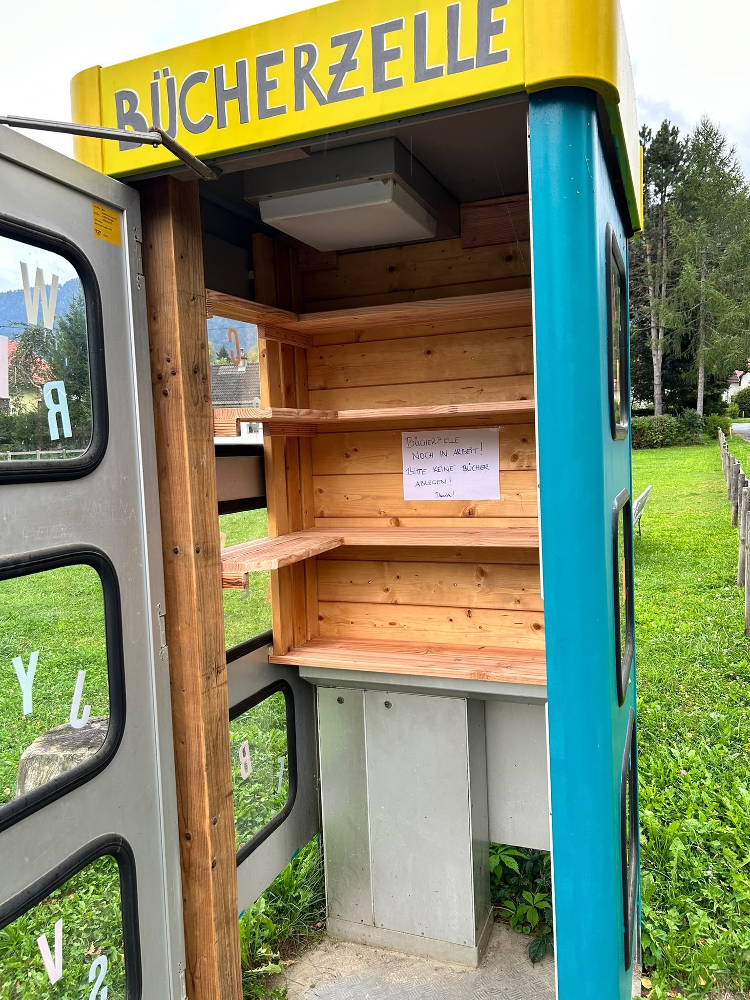 Büchertauschzelle in einer umgebauten Telefonzelle mit Hinweisschild in Österreich