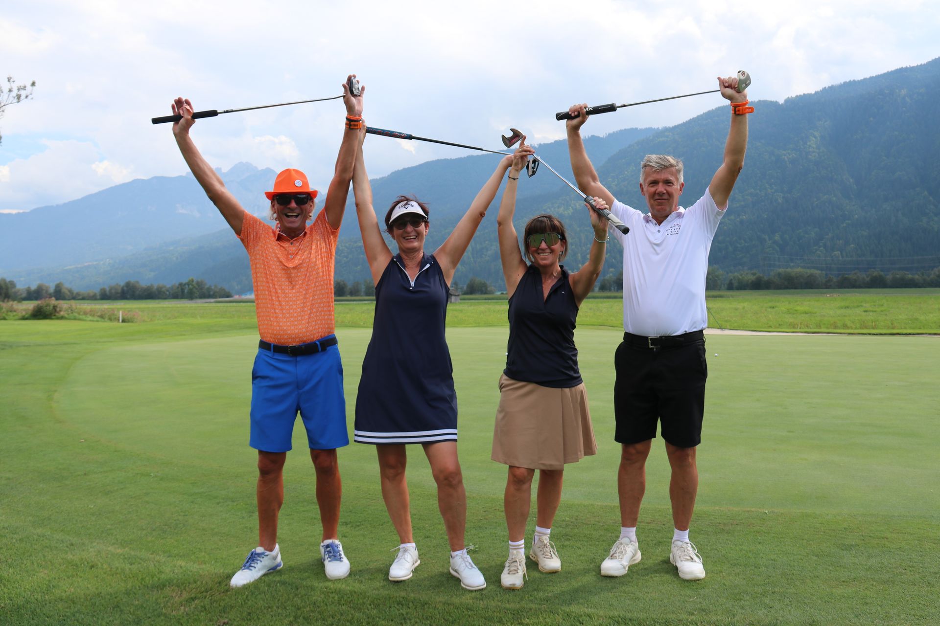 Golfspieler mit erhobenen Armen und Schlägern vor Bergkulisse in Österreich